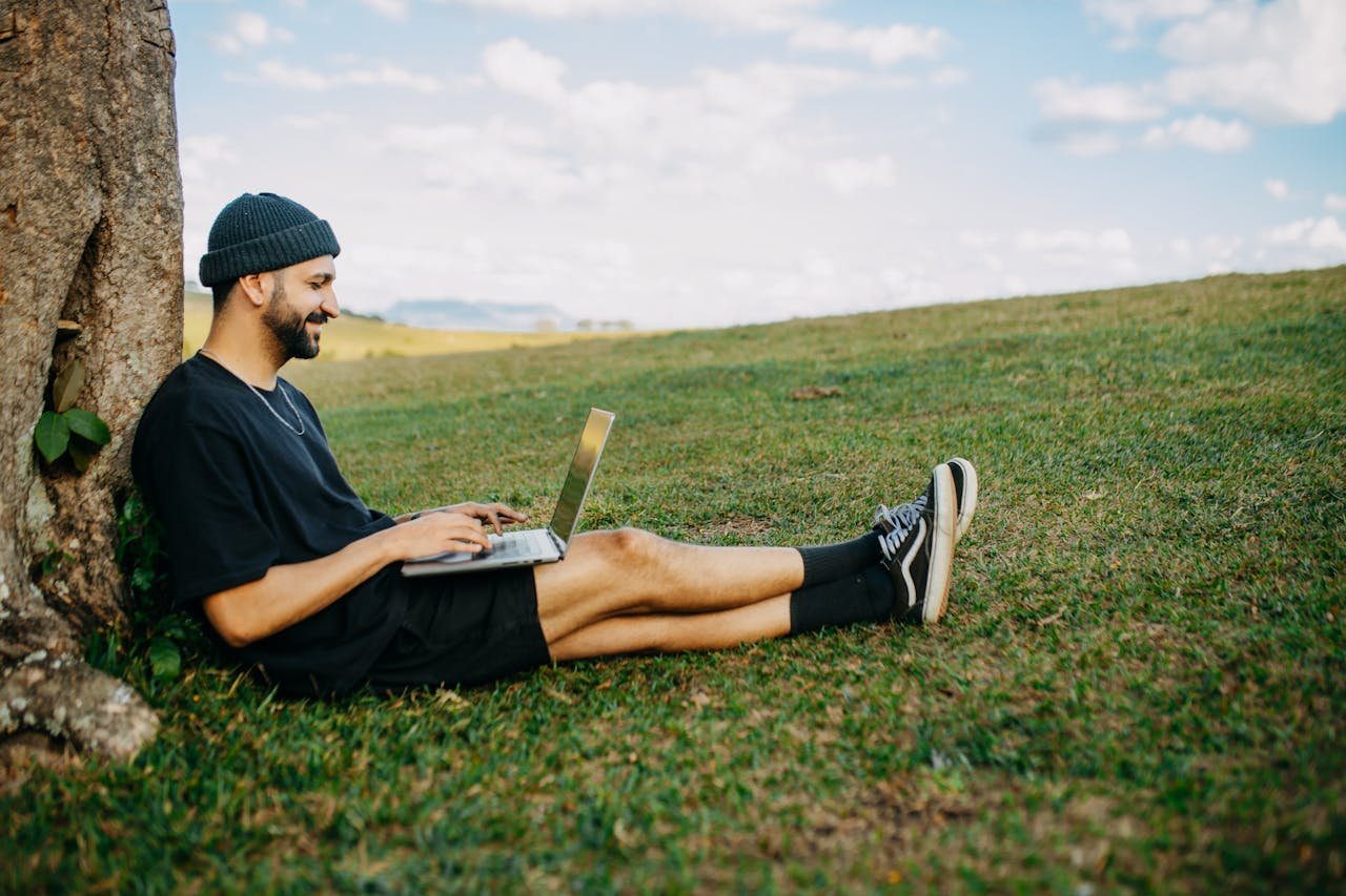 Man Sitting by Tree and Working on Laptop
